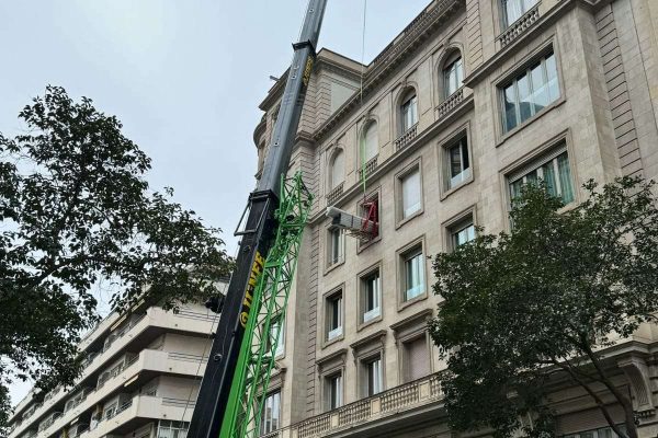 Grúa móvil de Grúas Junfe elevando carga en edificio.