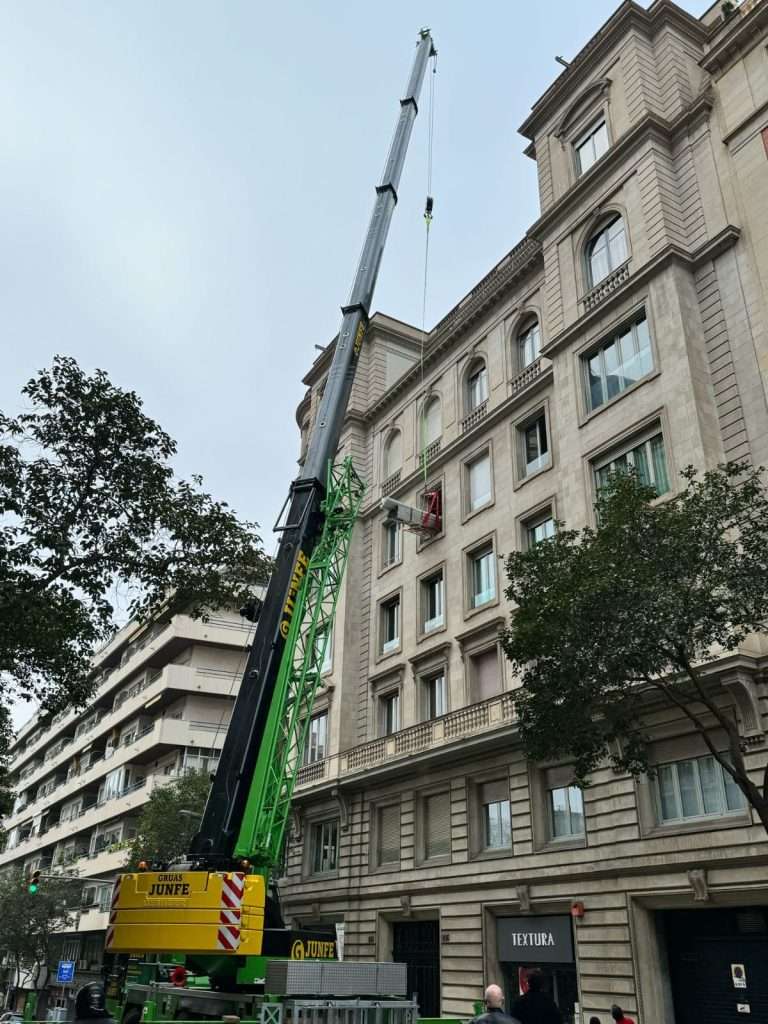 Grúa móvil de Grúas Junfe elevando carga en edificio.