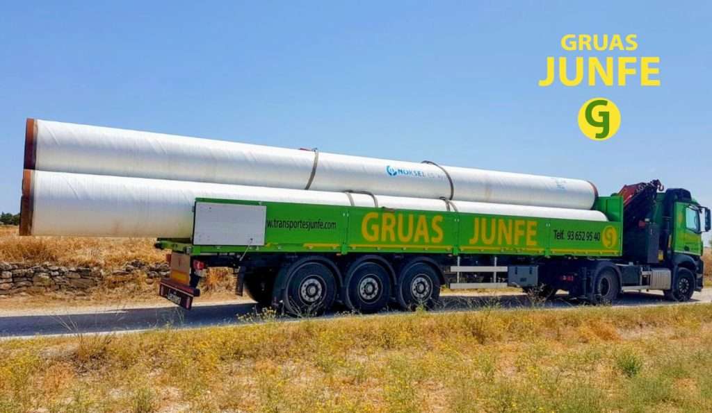 Camión grúa de Grúas Junfe transportando tuberías industriales sobredimensionadas en ruta, especial Barcelona.