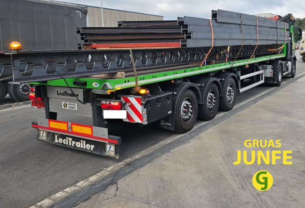 Camión de Grúas Junfe con plataforma Lecitrailer cargado con vigas y estructuras metálicas para transporte especial en Barcelona.