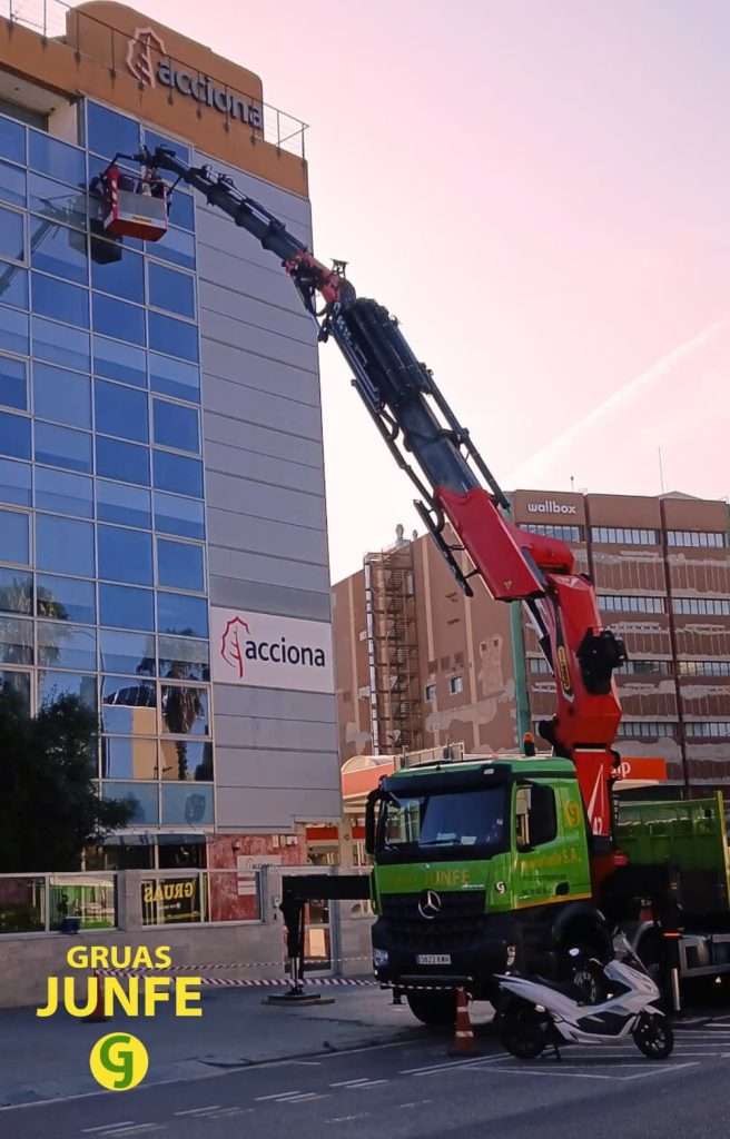 Camión grúa de Grúas Junfe con cesta de seguridad realizando limpieza de cristales en fachada de edificio de Barcelona.