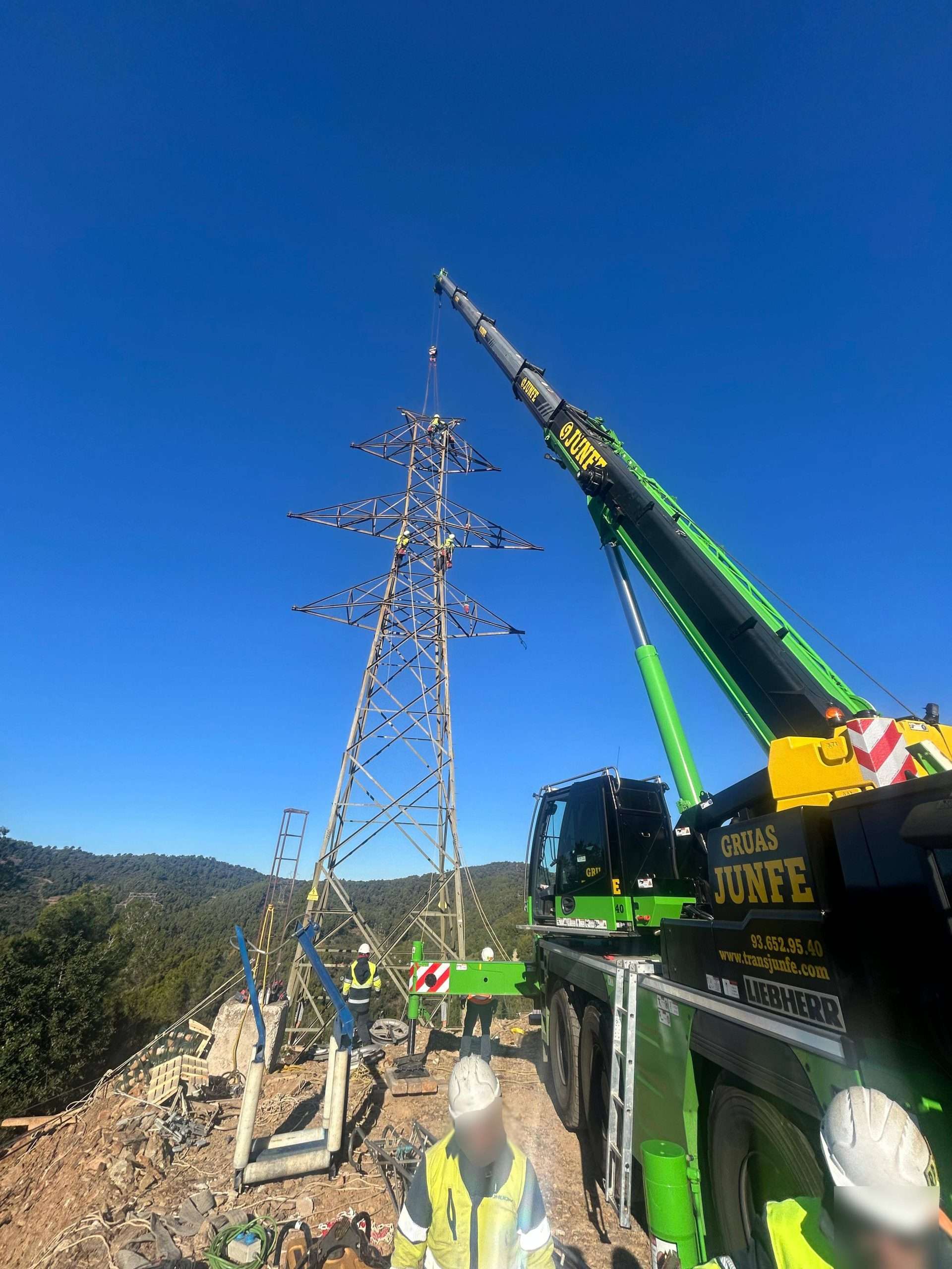 Operarios especializados trabajando en la cima de una torre eléctrica asistidos por una grúa de Grúas Junfe.