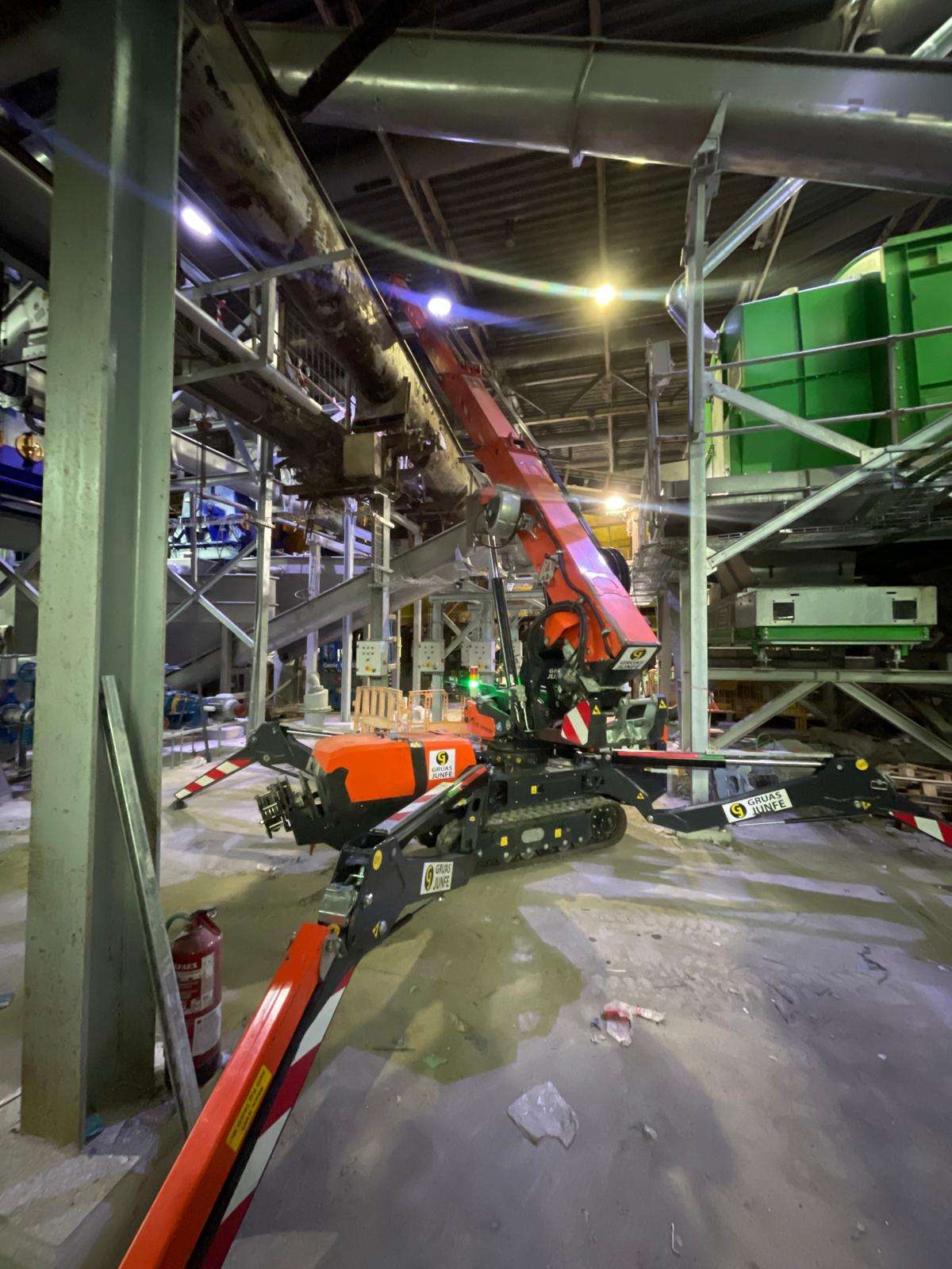 Minigrúa compacta elevando carga bajo estructuras metálicas y tuberías