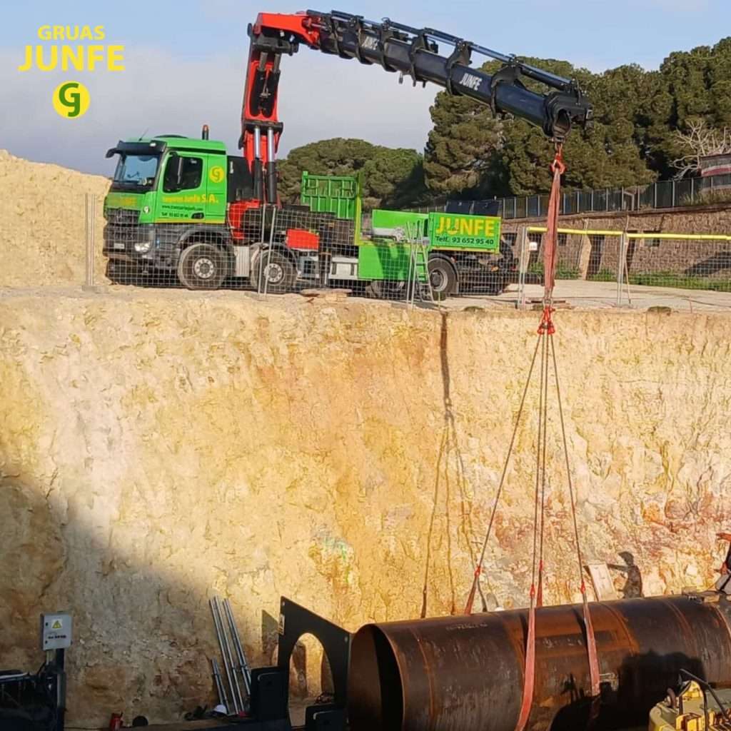 Camión grúa articulada de Gruas Junfe izando tubería de acero en gran excavación civil.